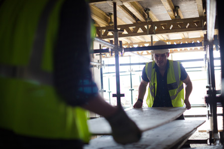 Two construction workers safely carrying a plank of wood