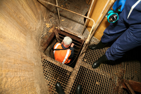 A construction worker climbing a ladder down into a confined space